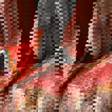 Person carving thin slices of meat from a jamon