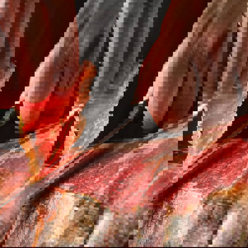 Person carving thin slices of meat from a jamon