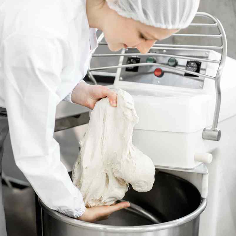 Baker Handling Dough In A Commercial Bakery