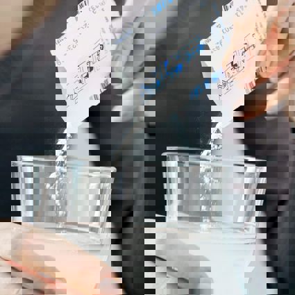 Person tipping soluble medicine into a glass of water