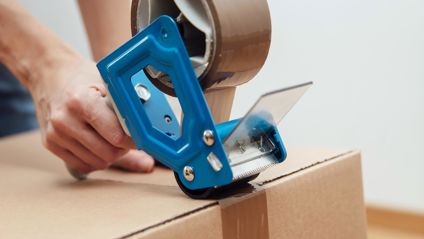 Person Taping A Cardboard Box Closed With A Tape Dispenser