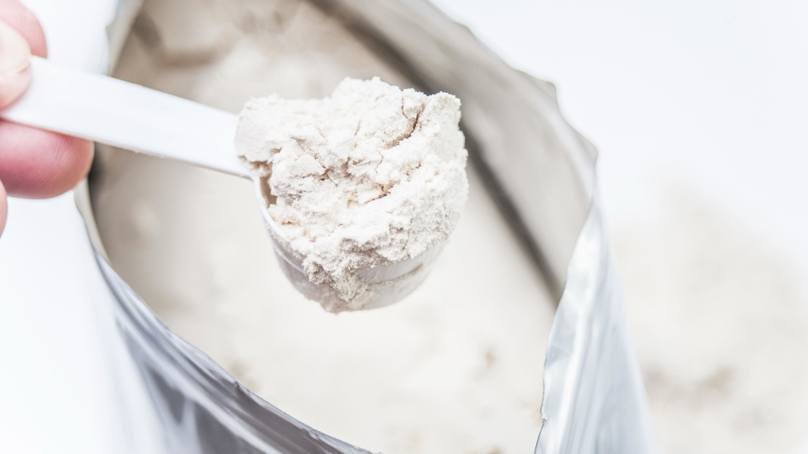 Person Scooping Protein Powder From A Bag
